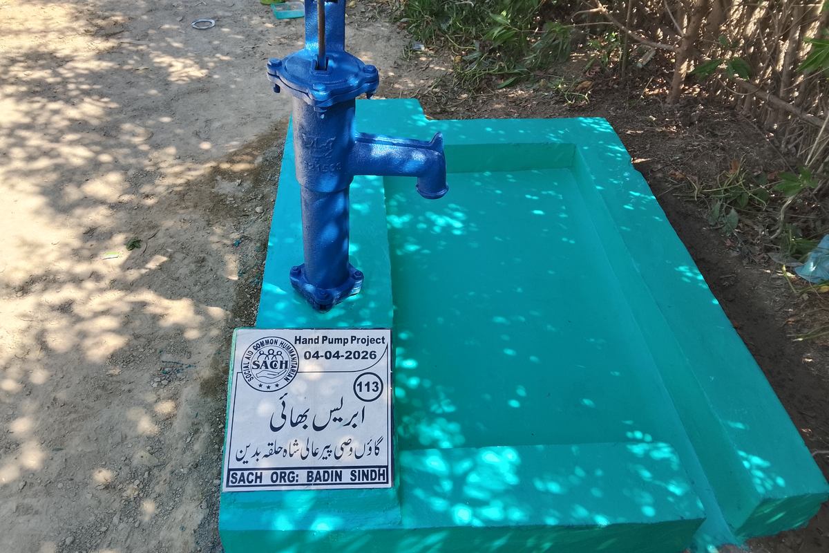 A completed SACH hand pump on a sealed concrete platform in rural Sindh